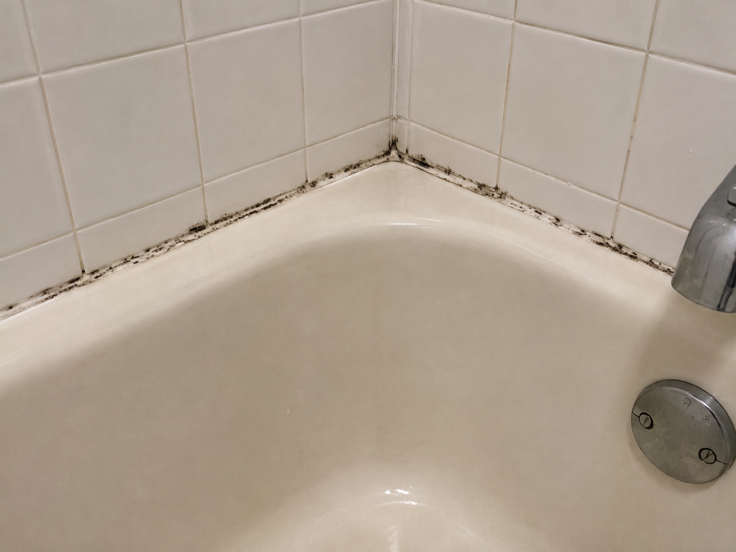 Bathtub with moldy caulk before removal - black mold growing along caulk lines